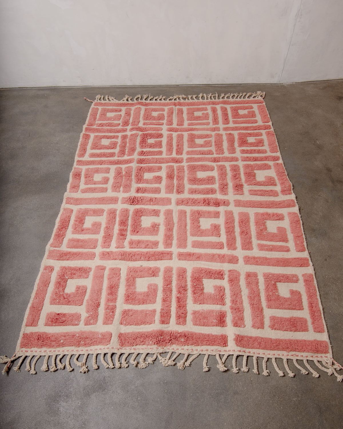Berberlin Beniourain rug with textural design made up of thick knotted wool pile in a soft dusty rose colour and flat woven base in natural cream, photographed on a concrete floor.